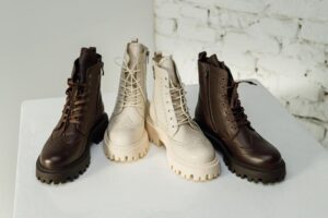 Four lace-up boots, all in pristine condition, are displayed on a white surface against a white brick wall. Two boots are dark brown, and two are beige. They feature rugged soles and a brogue design, making them the perfect new shoes for both style and durability.