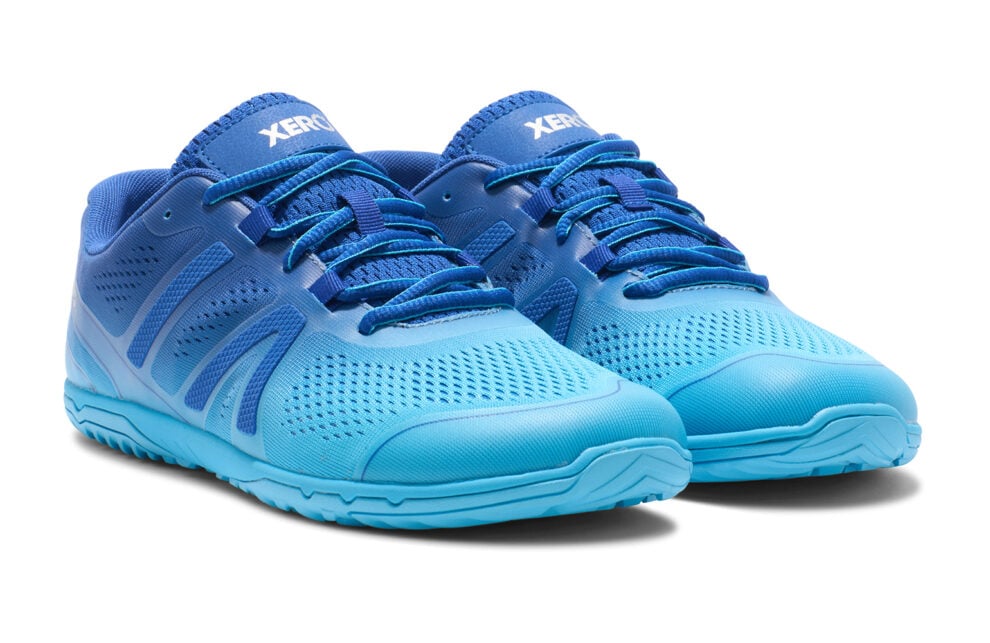 A pair of bright blue barefoot athletic shoes with a mesh design and textured soles offers comfort for digital nomads on the move. With blue laces and "XERO" on the tongue, these shoes sit against a plain white background.