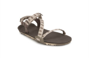 This sandal offers the comfort of barefoot shoes with a flat sole and open toe design. It features beige straps with a geometric pattern, a dark brown footbed, and an adjustable ankle buckle. Perfect for digital nomads, it has textured tread for reliable traction on the go.