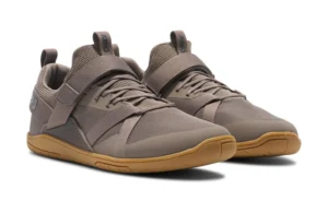 A pair of taupe athletic sneakers, inspired by performance footwear like the Forza Trainer, with mesh fabric uppers, elastic straps across the midfoot, and light brown rubber soles, displayed on a white background.