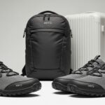 A pair of gray and black Xero Shoes—renowned as lightweight travel shoes—is placed in front of a black Xero backpack and a white hard-shell suitcase, all set against a neutral background.