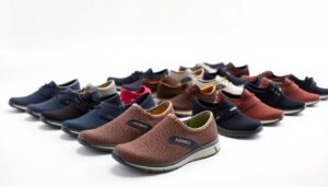 A variety of casual slip-on and lace-up shoes in multiple colors are arranged in rows on a white background. The focus is on the front row, featuring brown mesh slip-ons labeled "Xero Shoes" with the most cushion for all-day comfort.