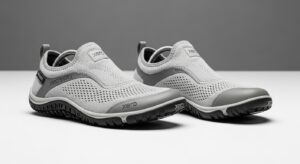 A pair of light gray slip-on athletic shoes with mesh uppers, rubber soles, and "Xero Shoes" branding offers all-day comfort and walking excellence, set against a plain gray and white background.
