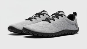 A pair of light gray, lace-up athletic shoes from Xero Shoes, featuring black soles, black laces, black inner lining, and a small circular logo on the heel area—showcasing quality craftsmanship on a plain light background.